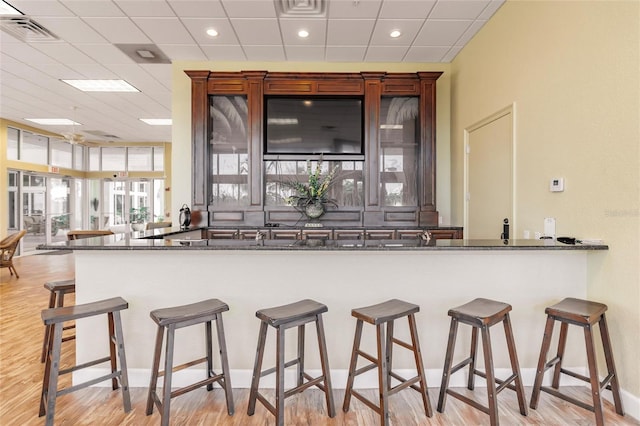 kitchen featuring light hardwood / wood-style floors, kitchen peninsula, a paneled ceiling, and a breakfast bar