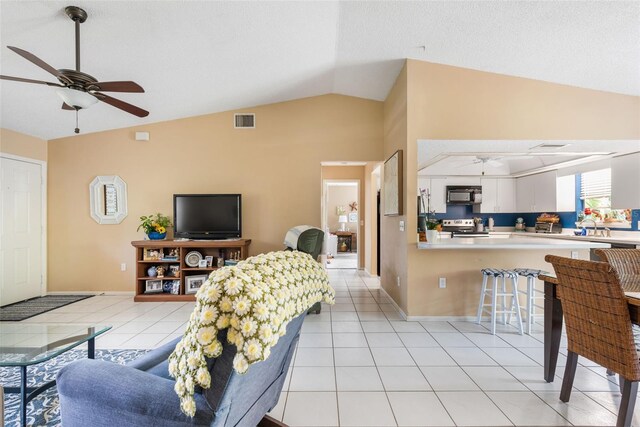 living room with ceiling fan, vaulted ceiling, and light tile patterned floors