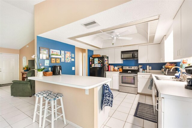 kitchen featuring a kitchen bar, a tray ceiling, black appliances, white cabinetry, and ceiling fan