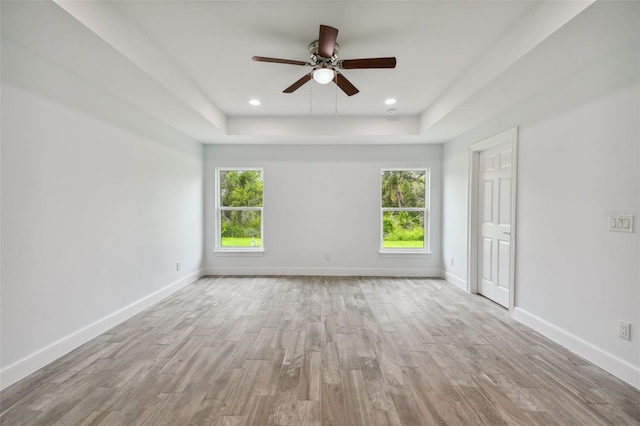 empty room with a tray ceiling, ceiling fan, and light wood-type flooring