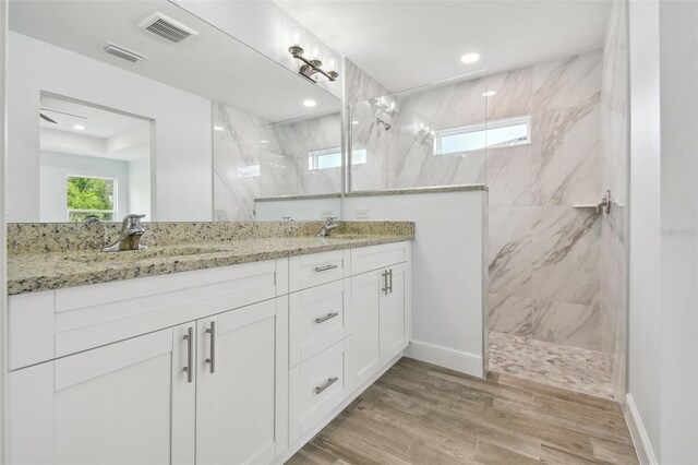 bathroom with a tile shower, hardwood / wood-style flooring, and dual bowl vanity