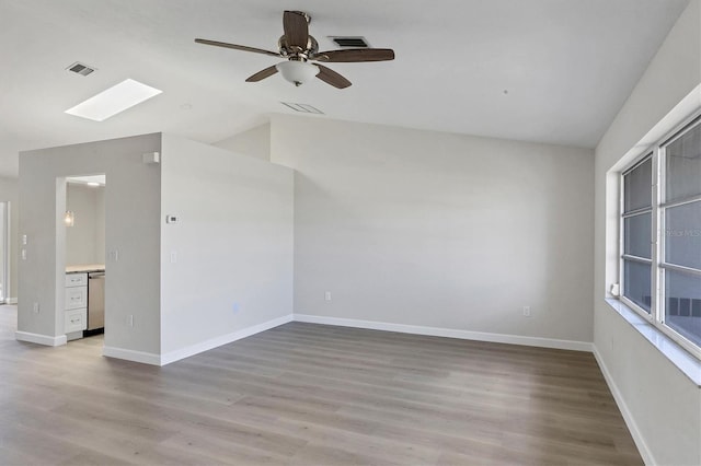 spare room with light wood-type flooring, visible vents, vaulted ceiling with skylight, and baseboards