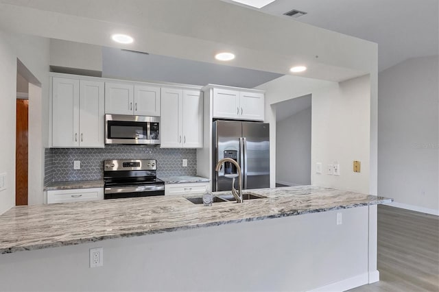 kitchen featuring light stone counters, stainless steel appliances, a sink, white cabinets, and decorative backsplash