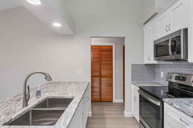 kitchen featuring a sink, light stone countertops, stainless steel appliances, white cabinetry, and backsplash