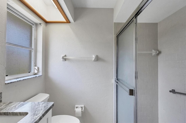 full bath featuring toilet, a textured wall, a shower stall, and vanity