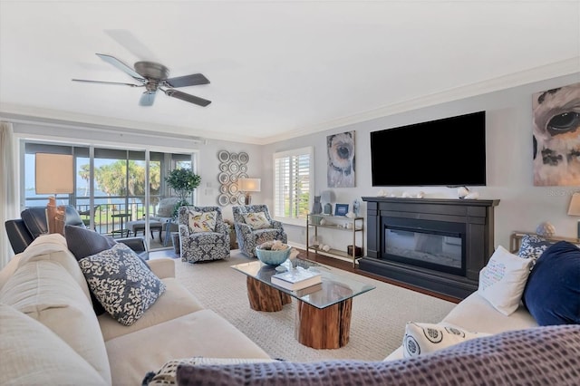 living room with ornamental molding, a ceiling fan, and a glass covered fireplace