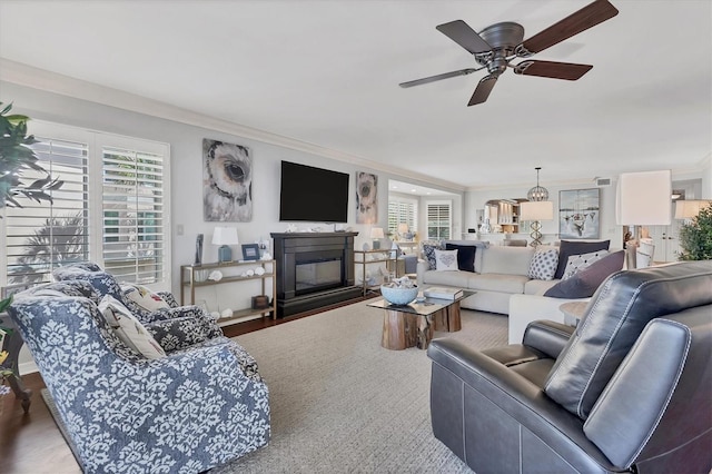 living area featuring ornamental molding, a glass covered fireplace, ceiling fan, and wood finished floors