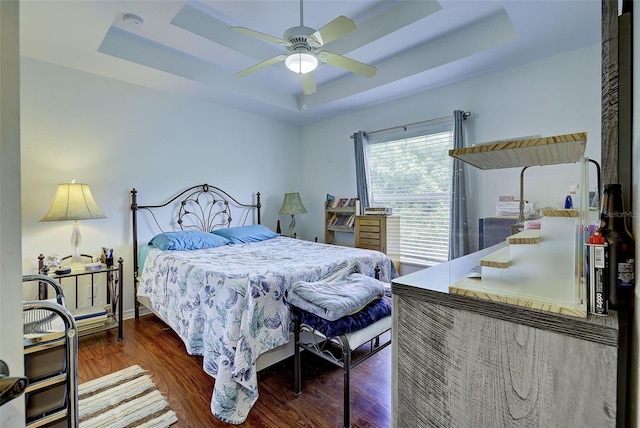 bedroom with hardwood / wood-style flooring, a raised ceiling, and ceiling fan