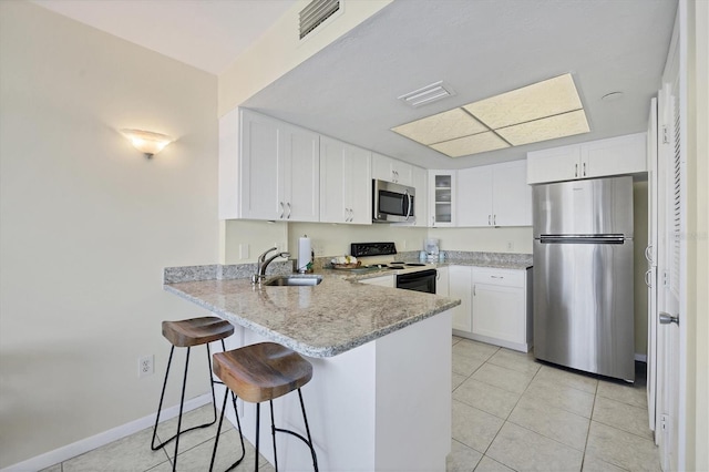 kitchen featuring light tile patterned floors, white cabinets, light stone counters, stainless steel appliances, and sink