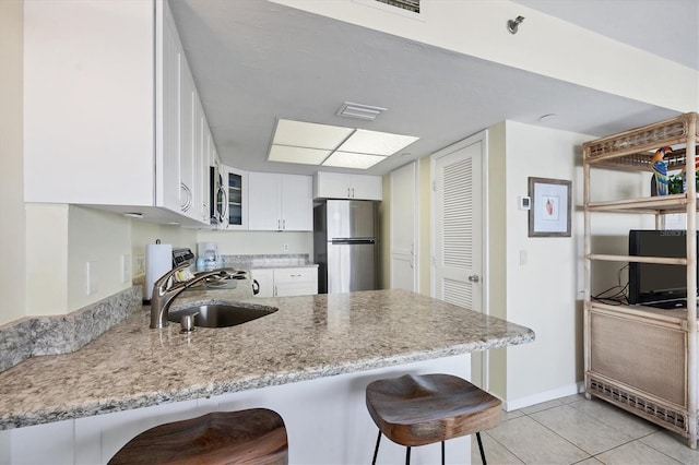 kitchen featuring stainless steel fridge, kitchen peninsula, light tile patterned floors, a kitchen breakfast bar, and white cabinetry