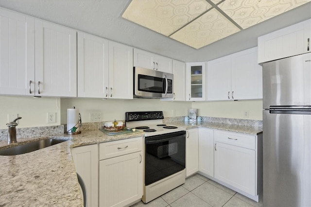 kitchen featuring white cabinets, stainless steel appliances, sink, light tile patterned floors, and light stone countertops