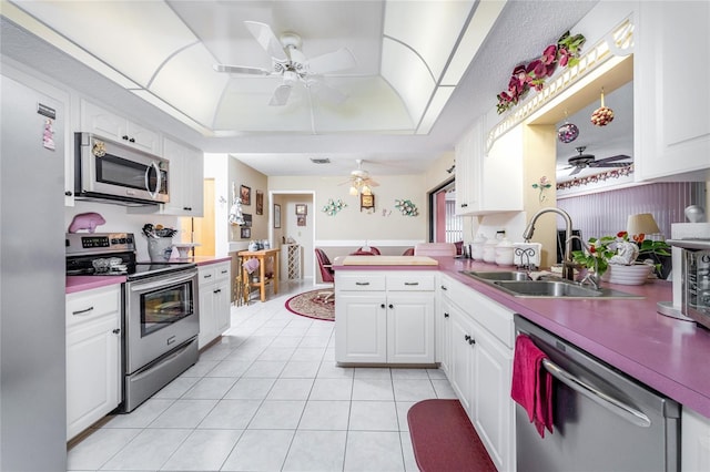 kitchen with light tile patterned flooring, stainless steel appliances, a peninsula, a sink, and a tray ceiling