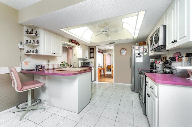 kitchen featuring ceiling fan, a peninsula, a skylight, appliances with stainless steel finishes, and open shelves