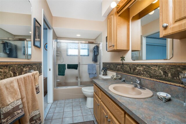 full bathroom featuring vanity, tile patterned floors, shower / bath combination with glass door, toilet, and a textured ceiling