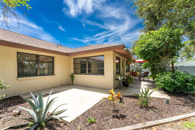 back of property with roof with shingles, a patio area, fence, and stucco siding