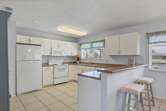 kitchen with white cabinetry, white appliances, light tile patterned floors, a textured ceiling, and kitchen peninsula