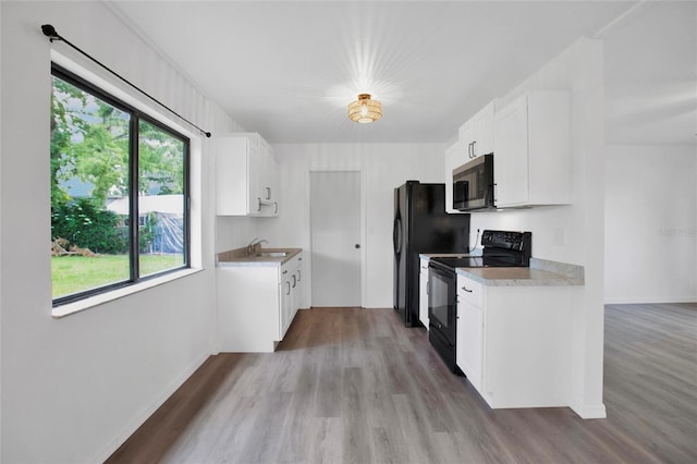 kitchen with black electric range oven, light hardwood / wood-style floors, sink, and white cabinets