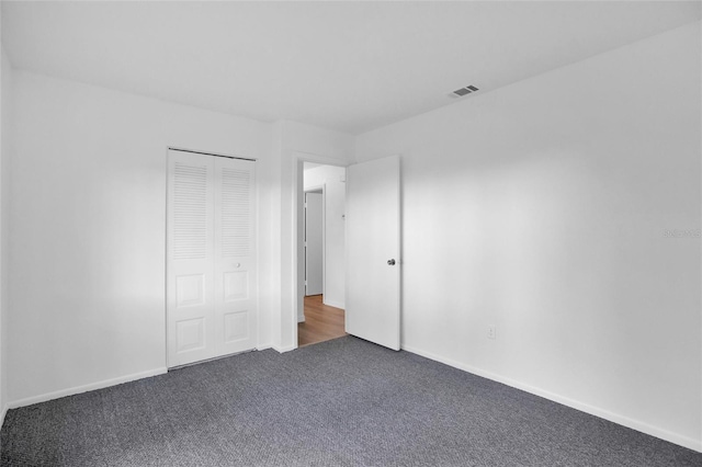 unfurnished bedroom with dark carpet and a closet