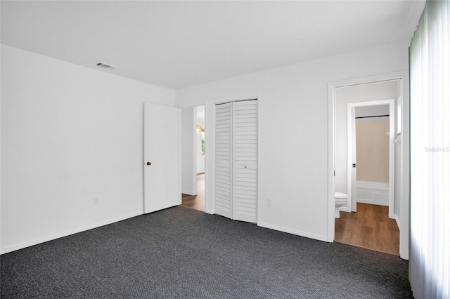 unfurnished bedroom featuring dark colored carpet, connected bathroom, and a closet