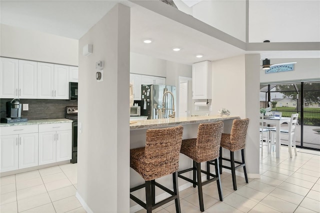 kitchen with stainless steel fridge with ice dispenser, a breakfast bar area, light tile patterned flooring, white cabinets, and decorative backsplash