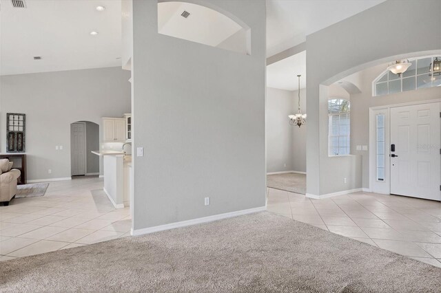 carpeted foyer with a chandelier and high vaulted ceiling