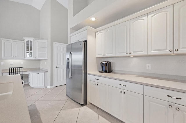 kitchen with stainless steel refrigerator with ice dispenser, lofted ceiling, light tile patterned floors, and white cabinets