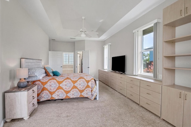 carpeted bedroom featuring a tray ceiling, multiple windows, ensuite bathroom, and ceiling fan