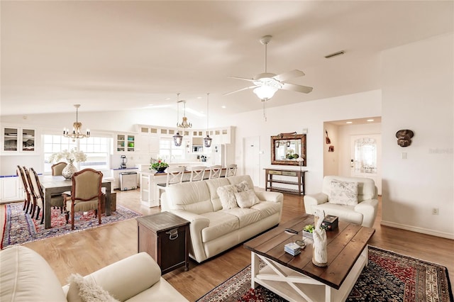 living room with lofted ceiling, wood-type flooring, and ceiling fan with notable chandelier