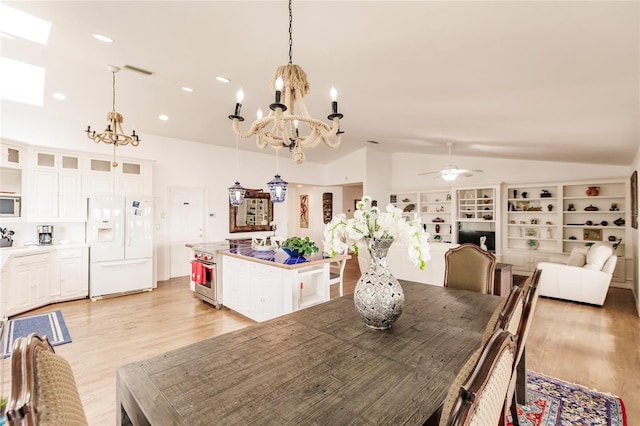 dining room with ceiling fan with notable chandelier, light hardwood / wood-style floors, vaulted ceiling, and built in shelves