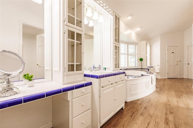 kitchen with sink, white cabinetry, light wood-type flooring, and vaulted ceiling