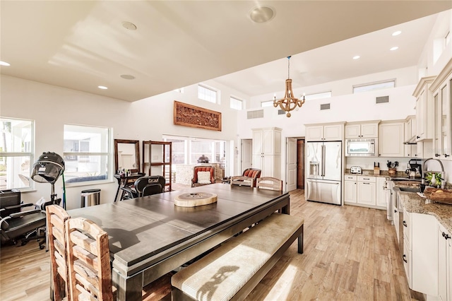 dining room with a high ceiling, light hardwood / wood-style flooring, sink, and an inviting chandelier