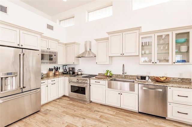 kitchen featuring sink, premium appliances, light wood-type flooring, and wall chimney exhaust hood