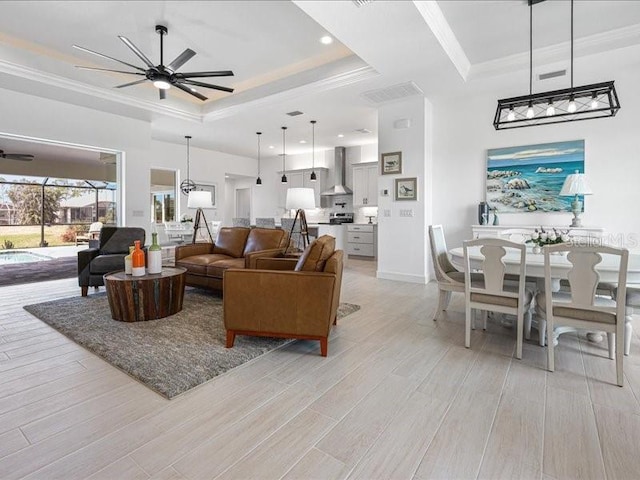 living room featuring crown molding, light wood-type flooring, ceiling fan, and a tray ceiling