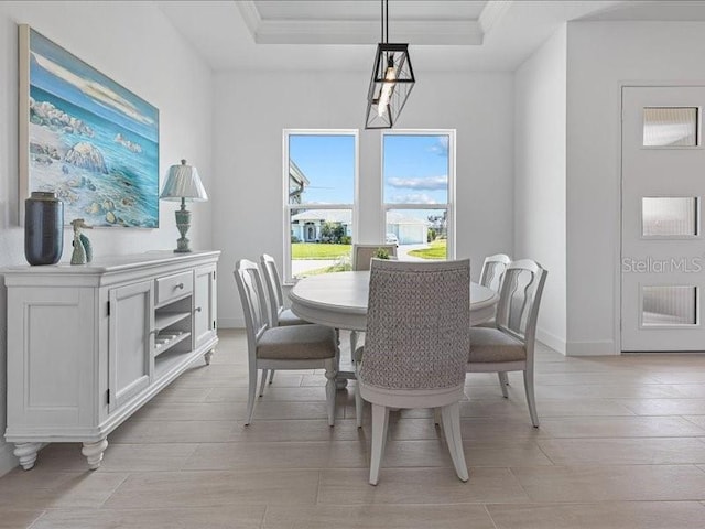 dining area with crown molding, a tray ceiling, and light wood-type flooring