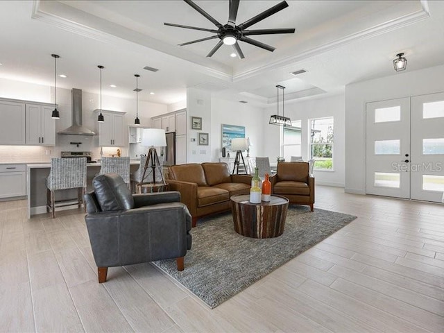 living room with french doors, ornamental molding, a raised ceiling, and light hardwood / wood-style flooring