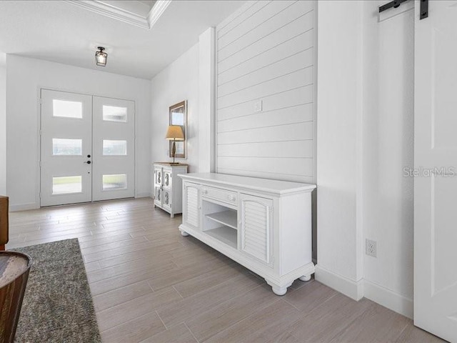 foyer featuring french doors, crown molding, a barn door, and light hardwood / wood-style flooring