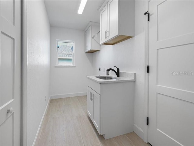 laundry room featuring cabinets, sink, and light hardwood / wood-style flooring