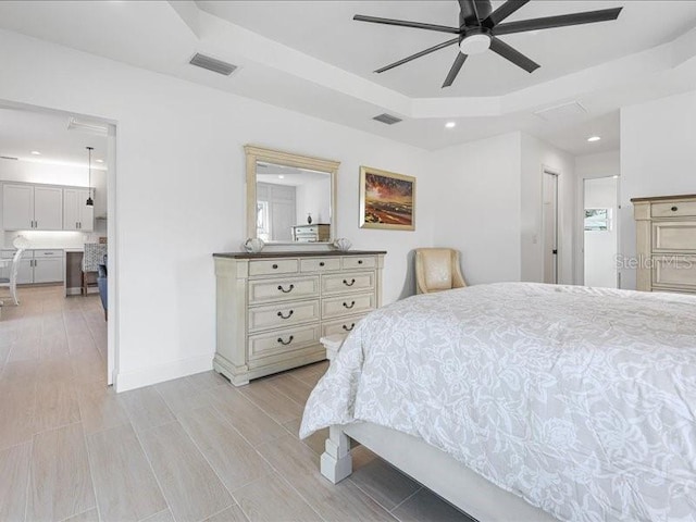 bedroom with ceiling fan, ensuite bath, and a tray ceiling