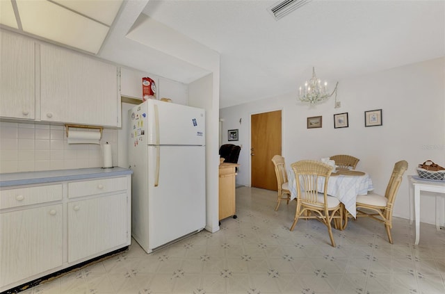 kitchen with white refrigerator, an inviting chandelier, hanging light fixtures, and backsplash