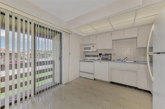 kitchen with white appliances, white cabinetry, sink, light tile patterned floors, and decorative backsplash