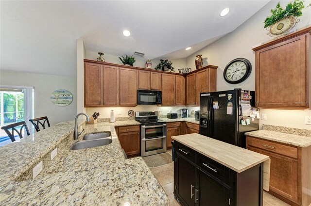 kitchen with a kitchen bar, kitchen peninsula, black appliances, light tile patterned floors, and sink