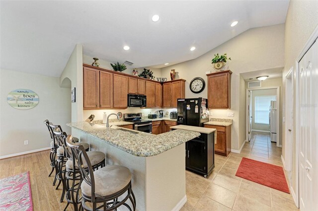 kitchen with light wood-type flooring, sink, black appliances, vaulted ceiling, and kitchen peninsula