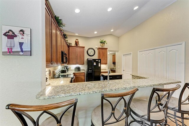 kitchen with lofted ceiling, kitchen peninsula, black appliances, light stone countertops, and sink