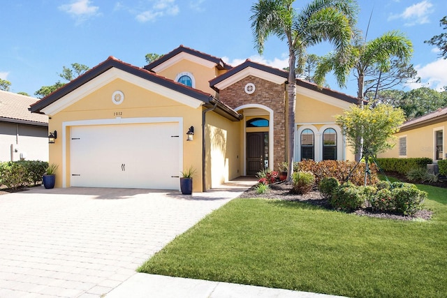 mediterranean / spanish home featuring a garage, decorative driveway, a front lawn, and stucco siding