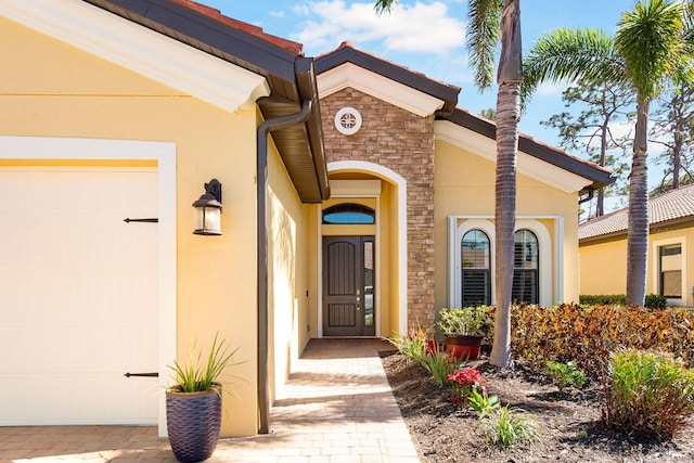 view of exterior entry featuring a garage, stone siding, and stucco siding