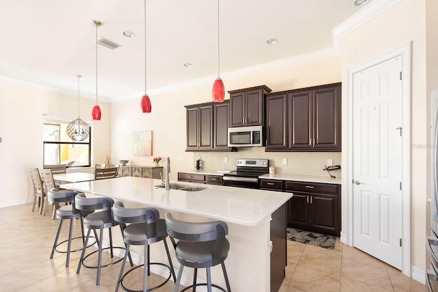 kitchen featuring a kitchen island with sink, a sink, hanging light fixtures, appliances with stainless steel finishes, and a kitchen bar