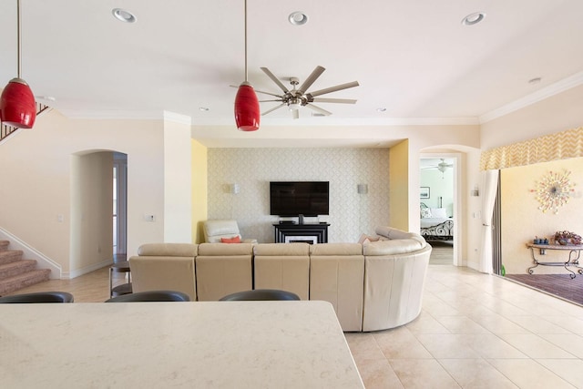 living area with an accent wall, arched walkways, crown molding, and ceiling fan