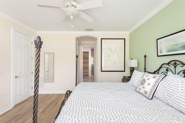 bedroom featuring arched walkways, crown molding, light wood finished floors, visible vents, and baseboards