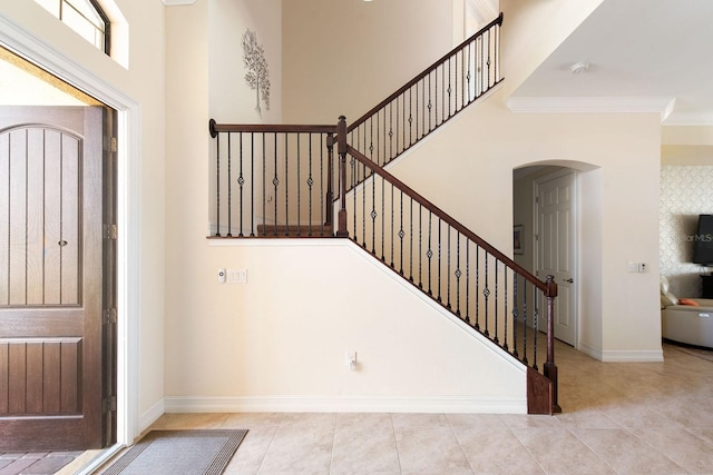 foyer with arched walkways, a towering ceiling, baseboards, and light tile patterned floors