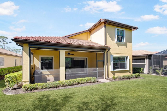 rear view of property with ceiling fan, a tile roof, a yard, and stucco siding